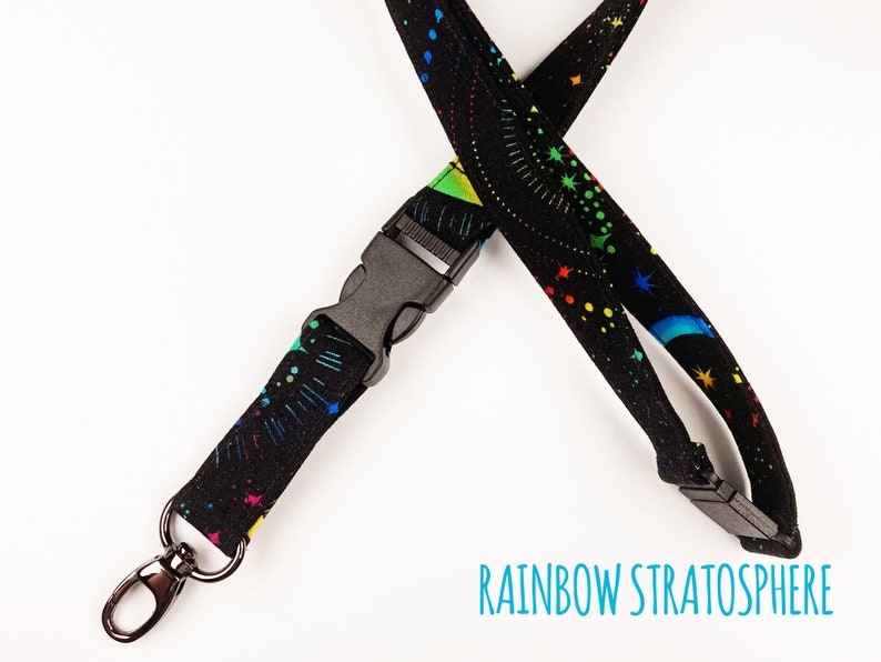 May include: Black lanyard with a rainbow and star pattern. The lanyard has a black plastic clip and a silver swivel hook.