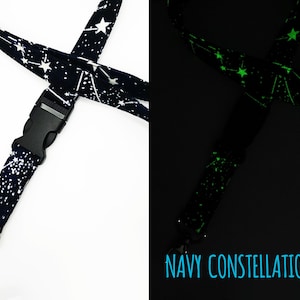 May include: A navy blue lanyard with white constellations that glow green in the dark. The lanyard has a black plastic clip and a silver swivel hook.  NAVY CONSTELLATIONS is printed on the lanyard.