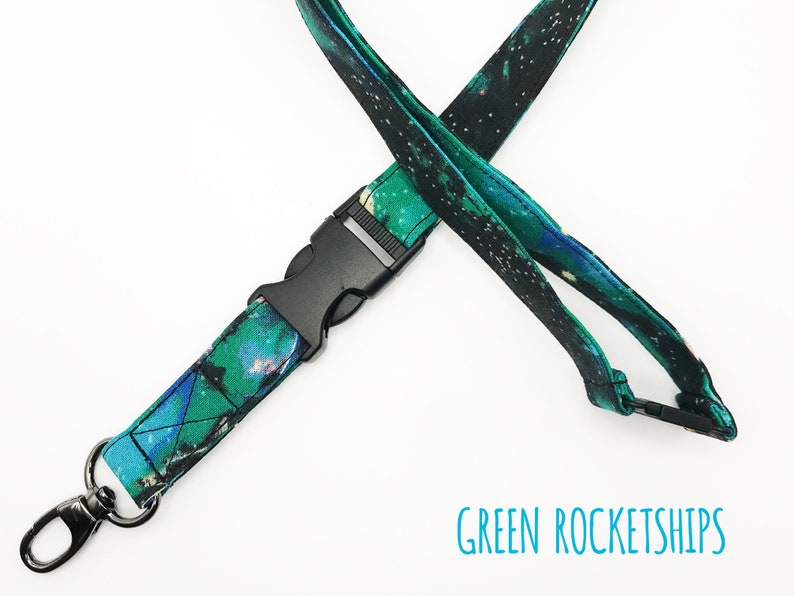 May include: A green and black lanyard with a galaxy print and a black plastic clip. The lanyard has a silver metal hook on one end. The text "GREEN ROCKETSHIPS" is printed below the lanyard.
