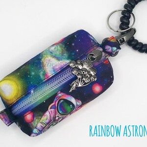 May include: A small zippered pouch with a rainbow astronaut and galaxy print. The pouch is attached to a black beaded keychain with a silver charm.