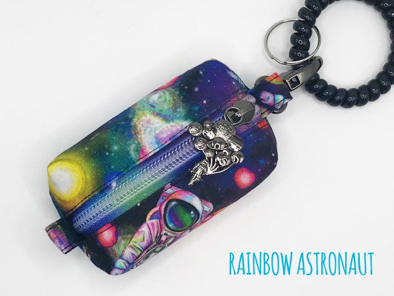 May include: A small zippered pouch with a rainbow astronaut and galaxy print. The pouch is attached to a black beaded keychain with a silver charm.