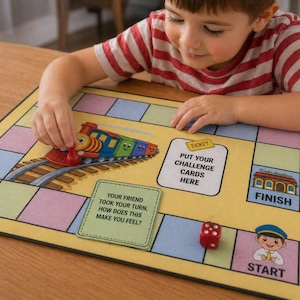 May include: A colorful children's board game with a train theme. The game board is yellow with colorful squares and features a toy train, dice, and text that reads "Put your challenge cards here".