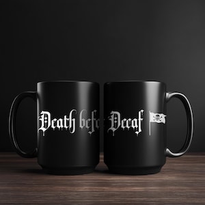 Peut inclure: Deux mugs à café noirs avec du texte gothique blanc qui dit "Death before Decaf". Un mug présente un drapeau blanc avec une tête de mort et des os croisés. Les mugs sont sur une surface en bois.