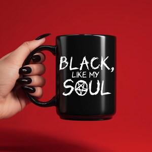 Peut inclure: Mug en céramique noire avec l'inscription blanche "BLACK, LIKE MY SOUL" en lettres gothiques. Le mot "SOUL" comporte un symbole de pentagramme. Le mug est présenté sur fond rouge.