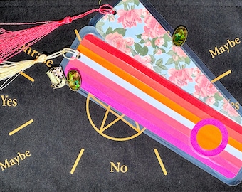 May include: Two decorative bookmarks with tassels and charms. One has a floral pattern, the other a rainbow design with an orange circle. The background is black with the words "Yes", "Maybe", and "No".