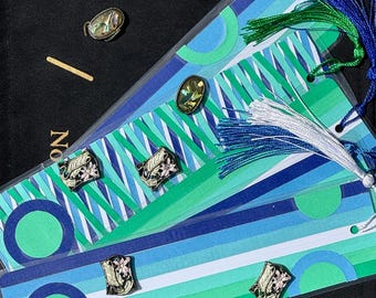 May include: Bookmarks with a blue, green, and white striped design, decorated with charms and tassels. The bookmarks have the words "Yes", "Maybe", and "No" printed on them. The charms are oval-shaped.