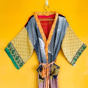 May include: A long-sleeved robe featuring a patchwork design with various patterns and colors including orange, blue, green, and cream. The garment has a wide collar, an open front with a tie belt, and wide sleeves with green floral borders.