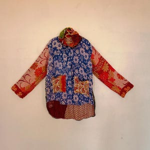 May include: A long-sleeved jacket featuring a patchwork design with various floral and geometric patterns in shades of blue, red, orange, and yellow. The garment includes a high collar, two front pockets, and visible stitching throughout.