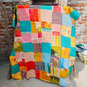 May include: A vibrant patchwork quilt, showcasing a mix of patterns and textures. The quilt is composed of squares in various colours, such as red, blue, yellow, and green. It is draped over a wooden frame.