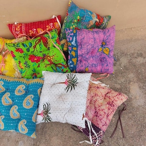 May include: A selection of vibrant square cushions with diverse patterns. The cushions display floral, paisley, and abstract designs in red, green, blue, and pink. Each cushion has a stitched edge and tie fastenings.