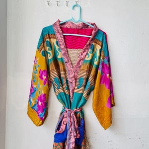 Può includere: Una vestaglia kimono a maniche lunghe caratterizzata da un vivace patchwork di colori tra cui giallo senape, magenta, verde acqua e rosa. Il capo presenta un mix di motivi floreali, disegni paisley e strisce geometriche con una cintura.