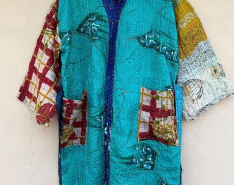 May include: A turquoise patchwork kimono-style robe with a quilted texture. The robe features a mix of patterned fabrics in red, yellow, and white. It has a blue trim and two front pockets. The sleeves are three-quarter length.