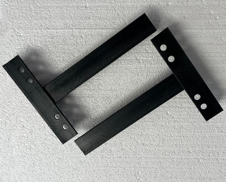 K&ouml;nnte beinhalten: Zwei schwarze Regalhalterungen aus Metall, jeweils mit einem langen horizontalen Arm und einer vertikalen Montageplatte. Die vertikalen Platten sind mit jeweils zwei kreisf&ouml;rmigen L&ouml;chern zur Befestigung versehen und bieten eine stabile St&uuml;tzstruktur.