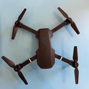 May include: A black drone with four propellers and a central body. The drone has a sleek design with a dark color scheme and white accent stripes on the arms. The propellers are angled and ready for flight.