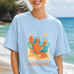 May include: A light blue t-shirt featuring a graphic of an orange lobster wearing blue headphones, sitting in a beach chair with a laptop and a tropical drink. The text OOO & Chill() is printed below the graphic in orange and blue lettering.