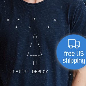 Op de afbeelding: Marineblauw t-shirt met een witte afbeelding van een kerstboom gemaakt van lijnen en sterren, en de tekst "LET IT DEPLOY". Het shirt wordt gedragen met een grijze beanie.