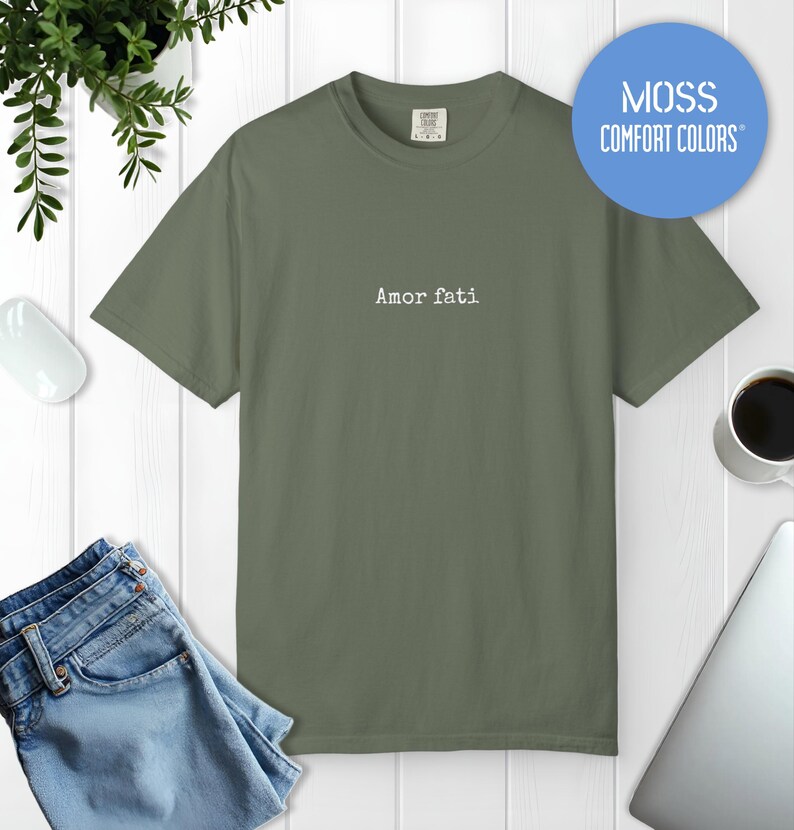 Peut inclure: Un t-shirt &agrave; manches courtes vert mousse avec le texte Amor fati imprim&eacute; en blanc au centre de la poitrine. Le v&ecirc;tement pr&eacute;sente une encolure ronde et une coupe standard. Un graphique circulaire bleu en haut &agrave; droite affiche MOSS COMFORT COLORS.
