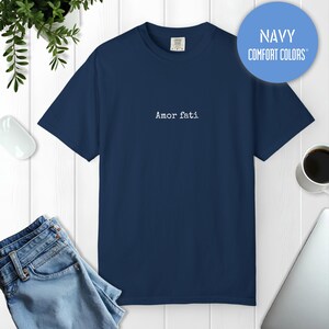 Peut inclure: Un t-shirt bleu marine &agrave; manches courtes avec le texte "Amor fati" imprim&eacute; en blanc au centre de la poitrine. Le t-shirt pr&eacute;sente une encolure ronde et une coupe standard. Un graphique bleu circulaire en haut &agrave; droite affiche "NAVY COMFORT COLORS".