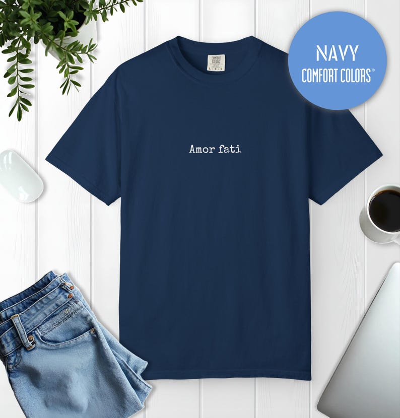 Peut inclure: Un t-shirt bleu marine &agrave; manches courtes avec le texte "Amor fati" imprim&eacute; en blanc au centre de la poitrine. Le t-shirt pr&eacute;sente une encolure ronde et une coupe standard. Un graphique bleu circulaire en haut &agrave; droite affiche "NAVY COMFORT COLORS".