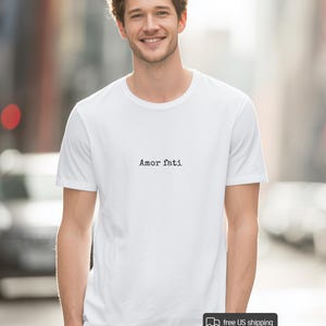 Peut inclure: Un t-shirt blanc &agrave; manches courtes avec le texte Amor fati imprim&eacute; en noir dans une police de style machine &agrave; &eacute;crire au centre de la poitrine. Le v&ecirc;tement pr&eacute;sente une encolure ronde classique et un ourlet droit pour un aspect &eacute;pur&eacute;.