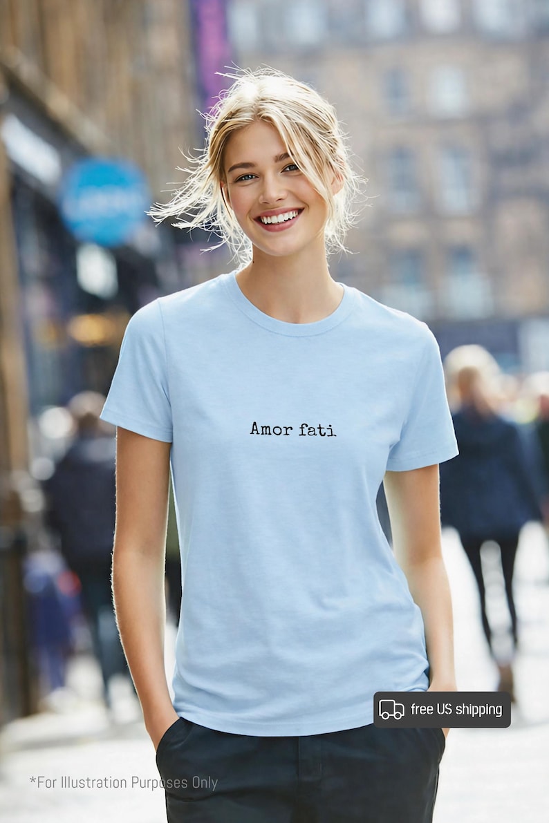 Peut inclure: Un t-shirt bleu clair &agrave; manches courtes avec le texte "Amor fati" imprim&eacute; en police de style machine &agrave; &eacute;crire noire sur la poitrine. Le v&ecirc;tement pr&eacute;sente un col rond classique et un ourlet droit, offrant une esth&eacute;tique simple et &eacute;pur&eacute;e.