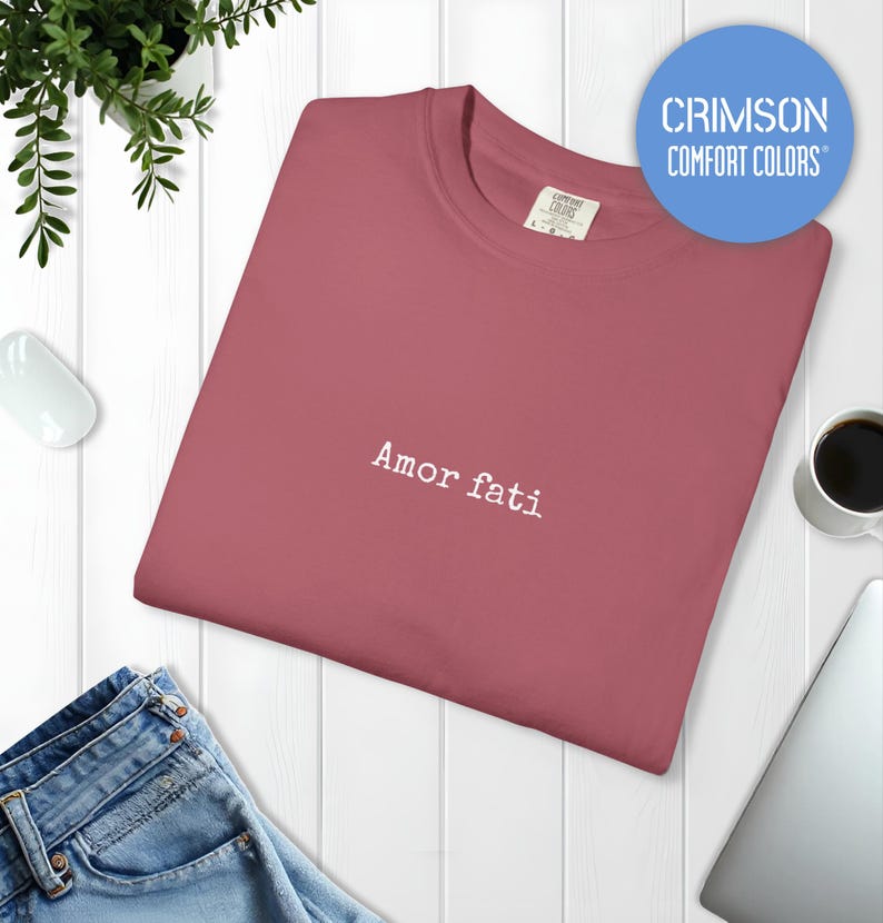 Peut inclure: Un t-shirt &agrave; col rond de couleur cramoisi avec le texte "Amor fati" brod&eacute; en fil blanc au centre de la poitrine. Le v&ecirc;tement pr&eacute;sente une &eacute;tiquette de marque Comfort Colors &agrave; l'int&eacute;rieur du col et un logo circulaire bleu.