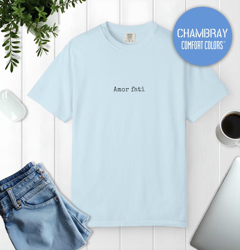 Peut inclure: Un t-shirt bleu clair &agrave; manches courtes avec le texte Amor fati imprim&eacute; en police noire de style machine &agrave; &eacute;crire au centre de la poitrine. Le v&ecirc;tement pr&eacute;sente une encolure ronde et une coupe standard, avec une &eacute;tiquette visible au col.