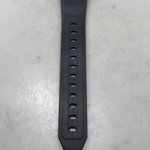 May include: A digital wristwatch with a black resin band. The watch face displays the time, 5:13, and other information. The band has a series of oval holes for adjustment.