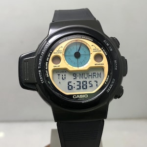 May include: Black Casio digital watch with a round face. The watch displays the time, date, and other functions. The watch has a black strap and a gold and blue face with the text "CASIO".