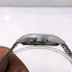 May include: A silver-toned wristwatch with a light blue face and a silver metal band. The watch has two buttons on the side and a clear plastic band holder. The watch is a classic style.