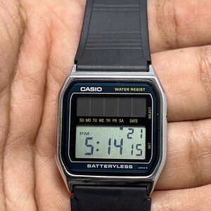 May include: A Casio digital watch with a black strap and a silver-colored face. The watch displays the time as 5:14:15 PM and the date as 21. The watch face has the text "CASIO", "WATER RESIST", and "BATTERYLESS".