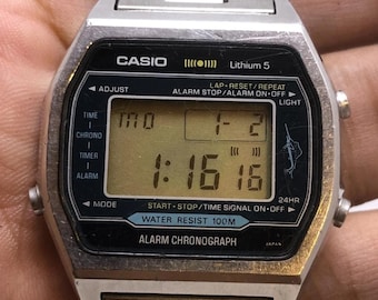 May include: A silver Casio digital watch with a black face displaying the time 1:16:16. The watch has a metal band and features buttons for adjusting time, alarm, and light. The watch face reads "Water Resist 100M" and "Alarm Chronograph."