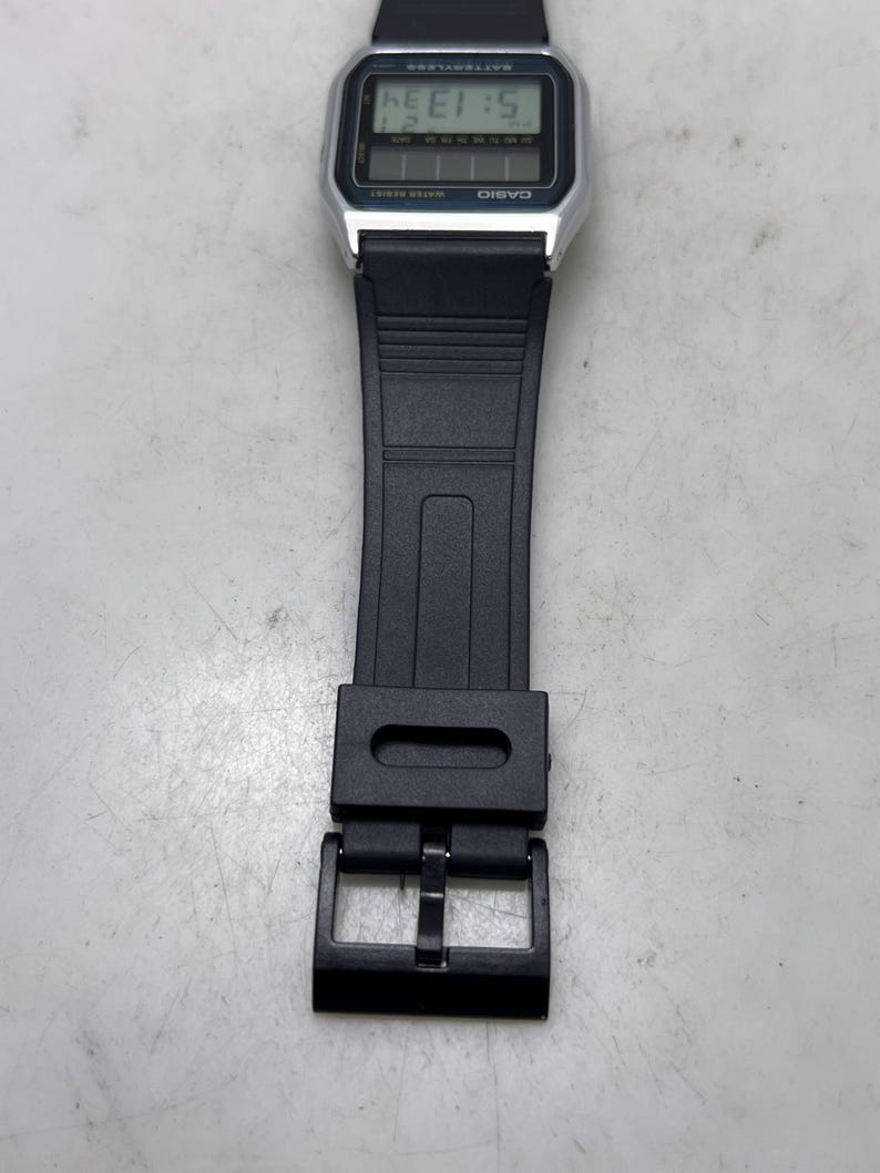 May include: A digital Casio watch with a black strap. The watch face displays the time and date in a digital format. The watch has a silver-colored case and a black buckle.