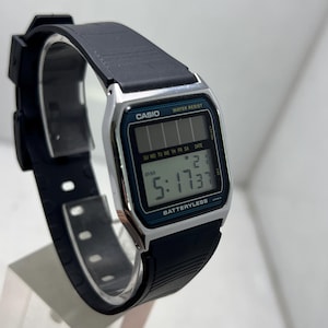 May include: A black Casio digital watch with a rectangular face. The watch displays the time as 5:17 PM and the date. The watch has a black band and a silver-colored bezel. The text "CASIO" and "WATER RESIST" are visible on the watch face.