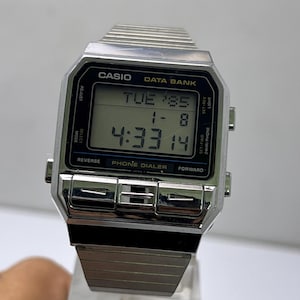 May include: A silver Casio Data Bank digital watch showing the time 4:33:14. The watch face displays Tuesday and the date 1-8. The watch has a rectangular face with buttons for adjustment and mode selection. The watch band is made of silver metal.