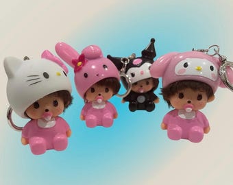 May include: Four small doll keychains featuring characters wearing animal-themed hoods. Two dolls wear pink bunny hoods, one wears a white cat hood, and one wears a black jester-style hood. Each doll has brown hair, a pacifier, and a pink outfit.