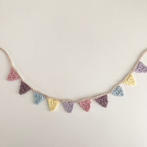 May include: A crocheted bunting with pastel coloured triangle flags. The bunting is strung on a natural twine string.