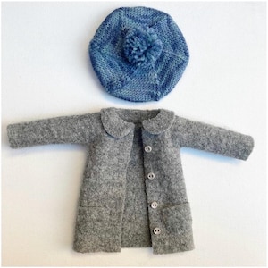 Peut inclure: Un manteau en feutre gris avec un col Claudine et cinq boutons sur le devant. Le manteau a deux poches en bas. Un béret bleu en tricot avec un pompon est posé sur le manteau.