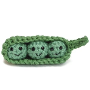 May include: Three green crocheted peas with smiling faces inside a green crocheted pea pod.