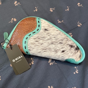 May include: A crescent-shaped clutch bag featuring a combination of brown embossed leather with floral patterns and white and black speckled hair-on hide. The bag is accented with turquoise leather trim and includes a black tag labelled MYRA.