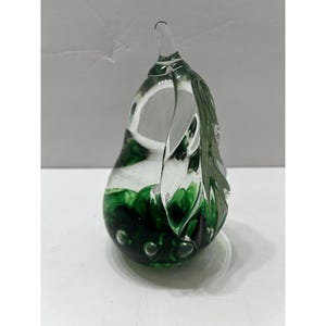 Puede incluir: Una escultura de vidrio transparente en forma de pera con un diseño verde y arremolinado en la base. La escultura tiene un acabado liso y pulido y una pequeña punta puntiaguda. El color verde se concentra en la parte inferior, creando un contraste visual llamativo.