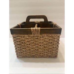 May include: A rectangular basket with a woven, light brown body and a dark brown wooden top and handle. The handle is centered and the basket is divided into sections. The top is secured with woven rope.