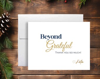 May include: A white thank you card with the words "Beyond Grateful" in navy and gold script. The card also includes the text "THANK YOU SO MUCH!" and a signature that says "Katia". The card is placed on a wooden surface with pine needles and pine cones.