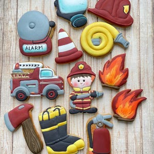 Peut inclure: Une collection de biscuits décorés en forme d'objets sur le thème des pompiers. Les biscuits comprennent un camion de pompiers, un pompier, des flammes, une alarme, un casque, des bottes, une hache, un extincteur, un cône de signalisation et une lance à incendie. Les biscuits sont décorés avec du glaçage rouge, jaune et bleu.