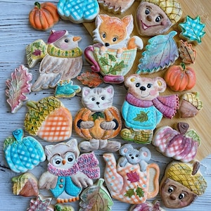 Peut inclure: Assortiment de biscuits sur le thème de l'automne, comprenant des citrouilles, des feuilles, des glands et des personnages d'animaux comme un renard dans une tasse à thé, un oiseau, un chat, un ours, un hibou et un koala. Les biscuits sont décorés de couleurs vives et de détails.