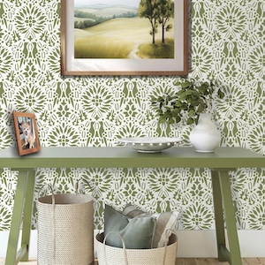 May include: A green console table with a white and olive green floral patterned wallpaper background. The table holds a white vase with green leaves, a white bowl, and a small wooden picture frame containing a photo of a dog.