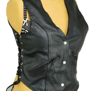May include: A black leather vest with a V-neck, featuring silver button closures and zippered pockets. The vest has a lace-up detail on the sides and is designed with a tailored fit. The vest is a classic biker style.