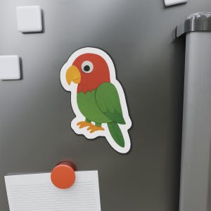 以下が含まれることがあります： 赤い頭、緑色の体、黄色のくちばしと足を持つ、カラフルなオウムのマグネット。鳥は白い縁取りのある漫画のイラストで、マグネットで灰色の表面に取り付けられています。