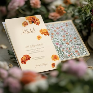 May include: Cream-colored wedding invitation with the word "Haldi" in elegant script, adorned with orange floral accents. The invitation includes event details: date, time, and location. The open invitation reveals a floral pattern.