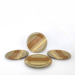 May include: Four ceramic plates with a striped pattern in shades of brown and yellow. The plates are oval and round, with a neutral background. The plates are likely for serving food.